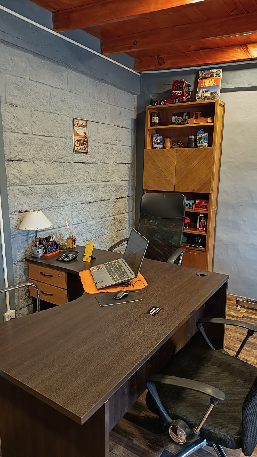 Escritorio de la oficina con una notebook y una biblioteca con camiones a escala